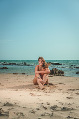 Fototapeta na wymiar Beautiful young European woman with an orange swimsuit sitting on a beach in Cádiz