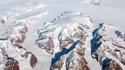 Aerial view of the frozen landscape covered in glaciers, rivers and icebergs on the south coast of Greenland from the window of an airplane from UK to San Francisco