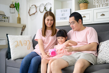 An asian family is teaching daughter on savings money with a piggy bank, financial planning concept