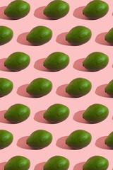 Trending style pattern of a whole green avocado on a pink background with hard light. Creative food texture.