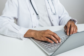 hands of an afro doctor using a modern laptop on the top of a white desk