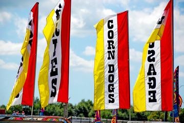 Obraz premium Bright yellow and red banners on poles advertising food for sale at a county fair