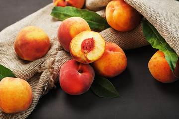 Peach fruit on a black background with a cloth of burlap and green leaves.