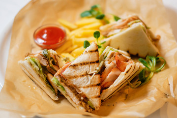Sliced chicken sandwich served with French fries and tomato ketchup. The concept of a delicious hearty homemade breakfast served in a restaurant.