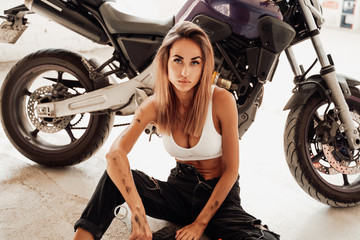 Fototapeta na wymiar An attractive girl in dirt sirring near sport moto bike