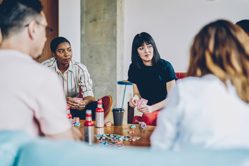 Youthful hipsters with alcohol beverages communicate about blackjack skills during leisure weekend for playing poker, friendly group of hostel guests gambling during cards gaming at gathering party