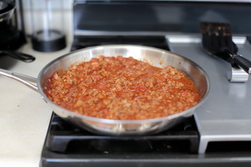 Bolognese sauce cooking in a stainless steel skillet.