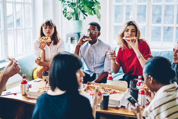 Hipster guys eating pizza spending free time together at home interior enjoying friendly company, young multicultural people dressed have party with Italian food and beer in modern apartment
