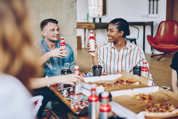 Fototapeta premium Hipster friends sitting at table with delivered pizza and alcohol drinks discussing board game with chips for playing poker during weekend, multicultural people enjoying gaming entertainment