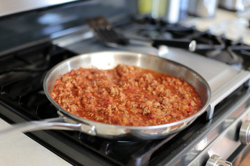 Bolognese sauce cooking in a stainless steel skillet.