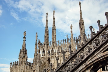 Fototapeta na wymiar Statue on spire of Milan Cathedral on blue sky background, Milan, Italy. Detail of Gothic roof overlooking Milano city in summer. Nice view of Milan from above