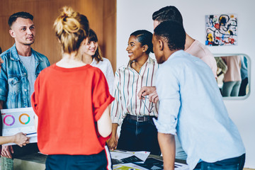 Team of cheerful and successful professionals 20s collaborating on common project, group of multicultural happy people in casual wear cooperating with each other discussing funny ideas indoors