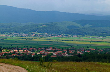 Naklejka premium Summer scene with meadow, forest, the Bulgarian villages Alino, Belchin near the ancient village Tsari Mali Grad and the mountains Rila and Verila, Bulgaria 
