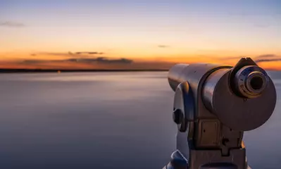 Fotobehang Een telescoop op een uitkijk bij een prachtige zonsondergang en een lange blootstelling van het water op de zee. © jaz_online