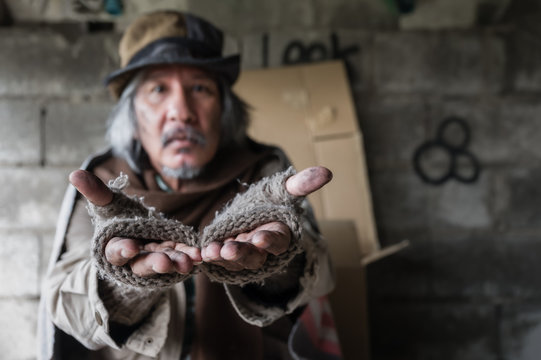 Closeup and focus to dirty hands of poor man beggar. Old homeless man with gray beard wear gloves with sitting and hands up for asking help and food beggar because hungry. Help and hope concept.