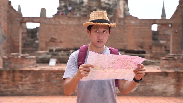 Young Asian man with hat looking at the map inside traditional temple in Ayutthaya Historical Park, Thailand.