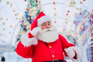 Portrait of an elderly man dressed as santa claus on the background of a christmas tree outdoors.
