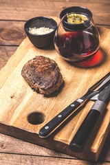Juicy medium Beef Rib Eye steak slices in pan on wooden board with fork and knife herbs spices and salt.