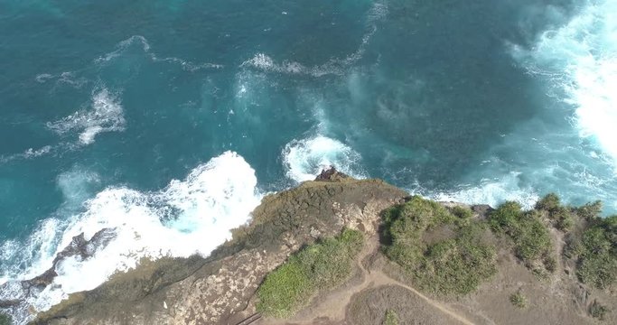 Overhead drone shot tilting down over waves breaking on rocky shore