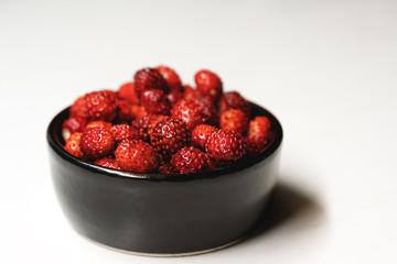 Fresh ripe dark red wild strawberries in a black bowl on a white background