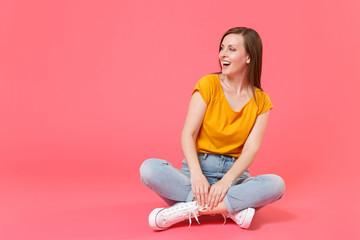 Full length portrait of cheerful funny beautiful attractive young brunette woman 20s wearing yellow casual t-shirt sitting on floor looking aside isolated on pink color wall background studio.