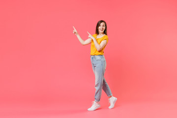 Fototapeta na wymiar Full length portrait side view of amazed excited young brunette woman 20s in yellow casual t-shirt pointing index fingers aside up on mock up copy space isolated on pink color wall background studio.