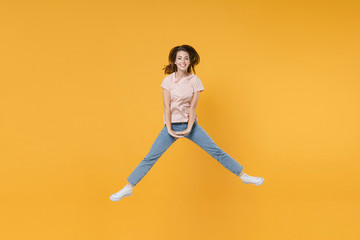 Fototapeta na wymiar Full length portrait of smiling cheerful funny young woman 20s wearing pastel pink casual t-shirt posing jumping spreading legs looking camera isolated on bright yellow color wall background studio.