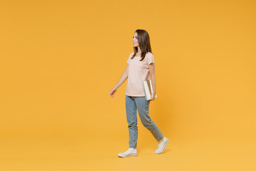 Fototapeta na wymiar Full length side view portrait of smiling young brunette woman 20s in pastel pink casual t-shirt posing hold laptop pc computer looking aside isolated on bright yellow color wall background studio.