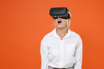 Shocked amazed young blonde female business woman girl 20s wearing white shirt watching in headset posing keeping mouth open isolated on bright orange color wall background studio portrait.