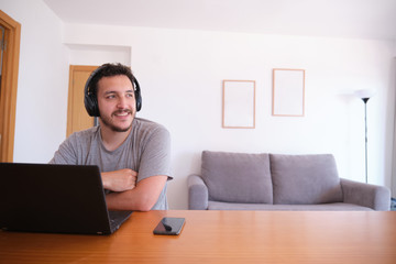 Young man wearing headphones watching series, videos, online classes on a laptop with the fan on. Studying online and e-learning concept.