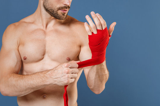 Cropped image young fitness sporty strong guy bare-chested muscular sportsman boxer isolated on blue background studio. Workout sport motivation lifestyle concept. Reeling up sports bandages on hand.
