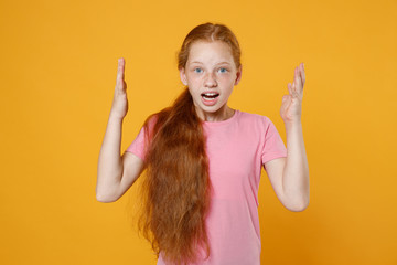 Shocked irritated little ginger redhead kid girl 12-13 years old wearing pink casual t-shirt posing spreading hands swearing isolated on bright yellow color wall background children studio portrait.