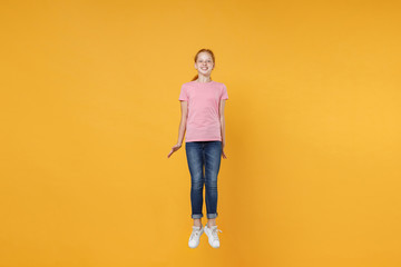 Fototapeta na wymiar Full length children studio portrait of cheerful little ginger redhead kid girl 12-13 years old wearing pink casual t-shirt posing jumping having fun isolated on bright yellow color wall background.