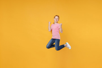 Fototapeta na wymiar Full length children studio portrait of happy little ginger redhead kid girl 12-13 years old in pink casual t-shirt posing jumping doing winner gesture isolated on bright yellow color wall background.