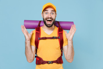 Amazed traveler young man in yellow t-shirt cap with backpack isolated on blue background. Tourist traveling on weekend getaway. Tourism discovering hiking concept. Keeping mouth open spreading hands.