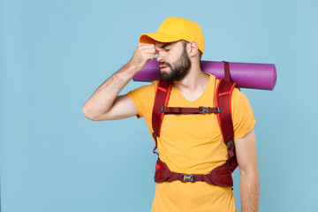 Tired traveler young man in yellow t-shirt cap with backpack isolated on blue background. Tourist traveling on weekend getaway. Tourism discovering hiking concept. Keep eyes closed, put hand on nose.