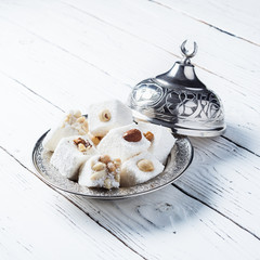 Turkish delight in a national metal plate with a lid and a crescent on a white wooden table.