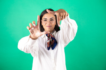 Naklejka premium Young beautiful business woman over isolated green background smiling making frame with hands and fingers with happy face