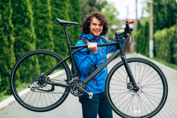 Outdoor half-length image of handsome hipster man holding his bike on the shoulder next to the...