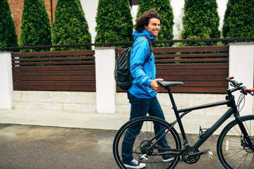 Horizontal outdoor shot of handsome man preparing for cycling on his bike down the street next to...
