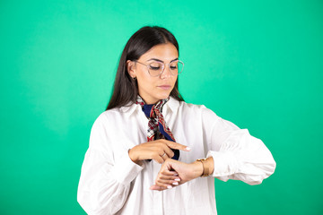 Young beautiful business woman over isolated green background smiling and pointing her watch