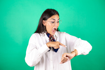 Young beautiful business woman over isolated green background surprised, looking and pointing his...