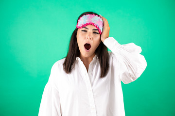 Young beautiful business woman wearing sleep mask over isolated green background Yawning tired covering half face, eye and mouth with hand. Face hurts in pain.