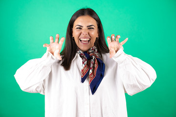 Young beautiful business woman over isolated green background smiling funny doing claw gesture as...