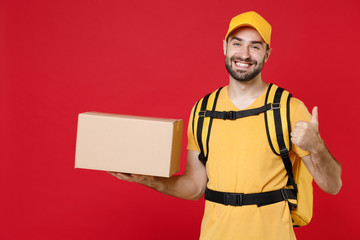 Delivery man in yellow cap t-shirt uniform thermal bag backpack with food hold cardboard box isolated on red background studio Male employee work as courier Service coronavirus covid-19 virus concept
