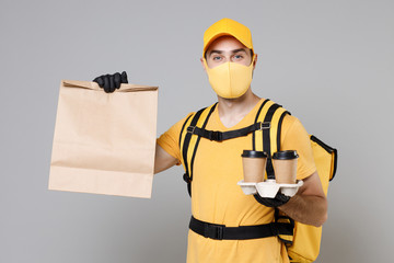 Delivery employee man in yellow cap face mask gloves tshirt thermal backpack hold craft paper takeaway food bag work courier service during quarantine covid-19 virus isolated on grey background studio