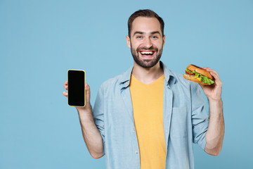 Cheerful young bearded man 20s in casual clothes posing hold american classic fast food burger...