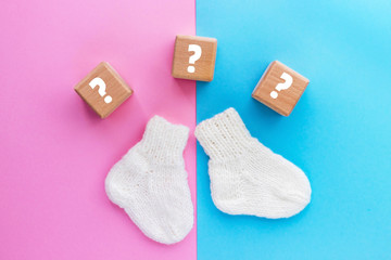 Wood cubes with question marks and pair of cute knitted baby socks on yellow-blue background. Gender of the baby. Boy or girl. Waiting foa a child. Newborn concept.