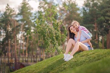 Naklejka na ściany i meble Mom and daughter are hugging in the park close-up and copy space. Sisters in nature. Mother's day, women's holiday. 