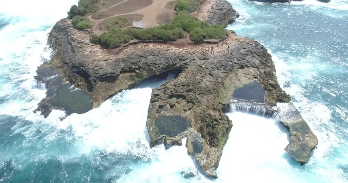 Drone shot flying backwards and tilting up to reveal waves crashing on a rocky coast